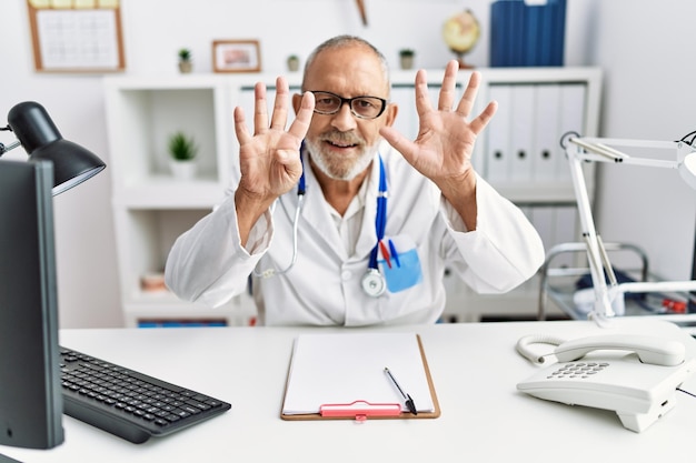 Mature doctor man at the clinic showing and pointing up with fingers number nine while smiling confident and happy