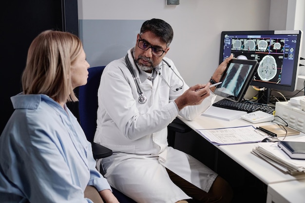 Зрелый врач показывает рентгеновское изображение пациенту
