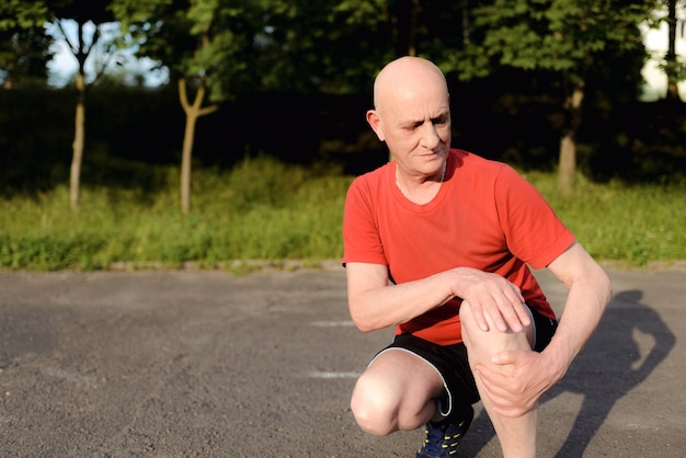 mature, elderly man sitting in the park and touching his knee by the pain during the day.