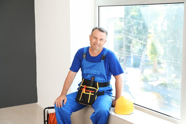 Mature electrician sitting on window sill in flat