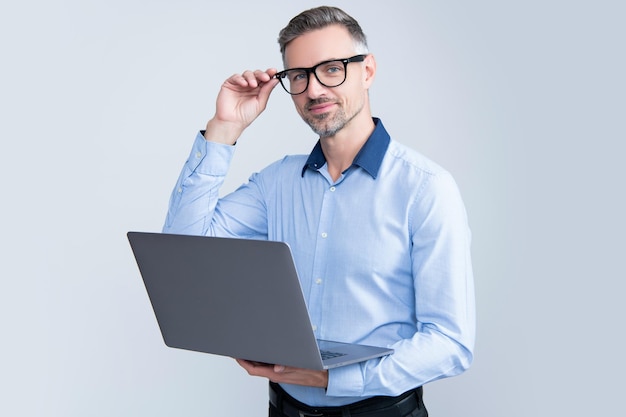 灰色の背景でコンピューターに取り組んでいる眼鏡の成熟した起業家