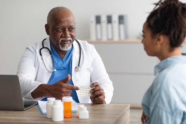 Mature experienced black doctor showing pills to pregnant lady