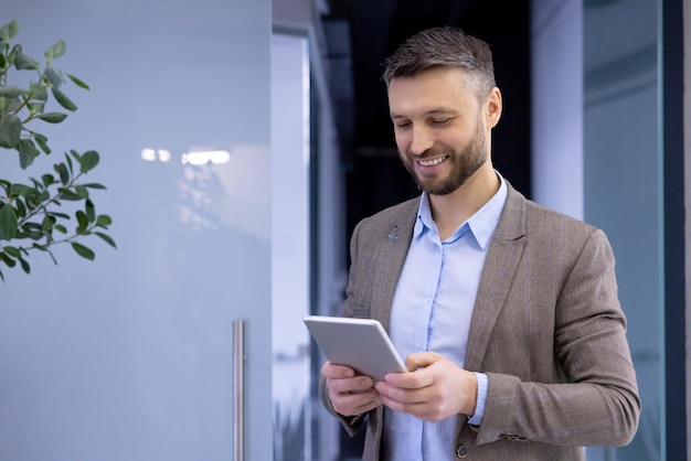 Mature experienced businessman inside office smiling contentedly senior man holding tablet computer