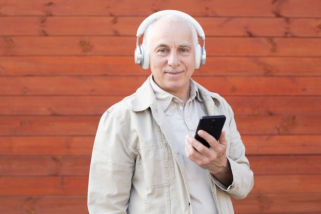 Mature fashion male having fun with new trends technology. Trendy senior man using smartphone app with red background. Tech and joyful elderly lifestyle concept