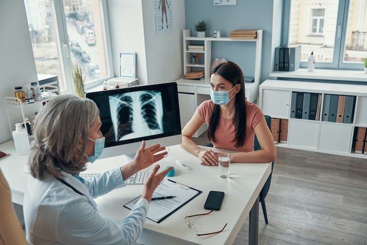Photo mature female doctor in white lab coat talking to young woman while sitting in her office