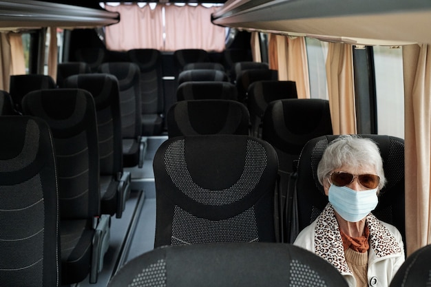 Mature female in protective mask sitting on seat inside bus