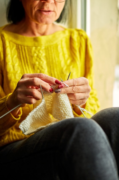 Mature female sitting on the windowsill and knitting