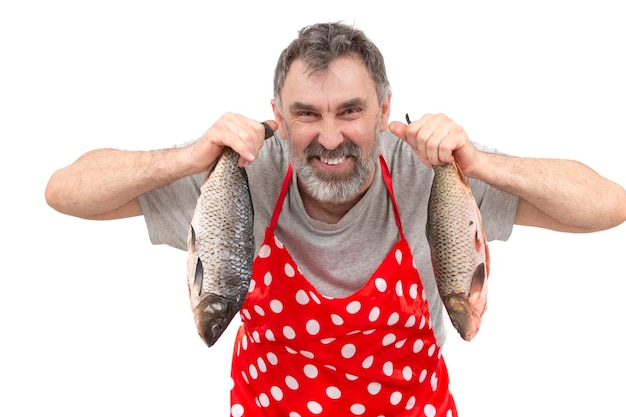 Mature fishmonger in red apron holding big freshwater fish and looking at camera on white background