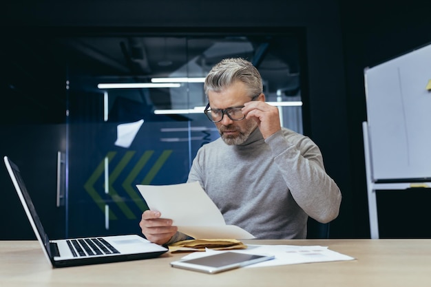 Mature grayhaired businessman inside modern office received letter message senior man upset opens