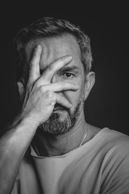 Uomo maturo dai capelli grigi nasconde il viso coperto con la mano che sembra triste o spaventato uomo di mezza età bello in foto in bianco e nero ritratto in bianco e nero di un uomo serio e bello attraente