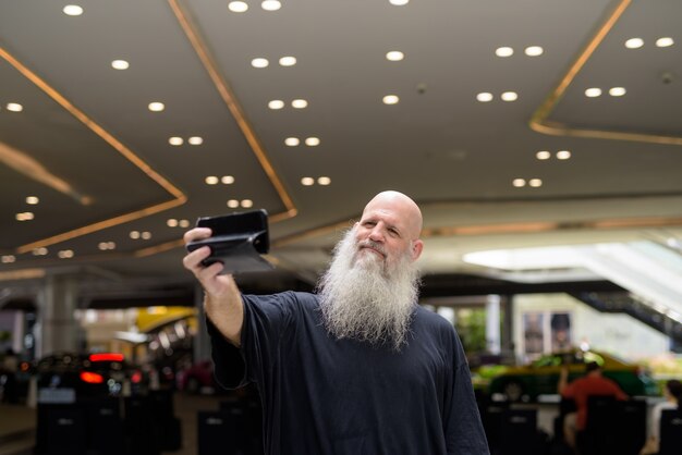 Mature handsome bald bearded man taking selfie in the city outdoors