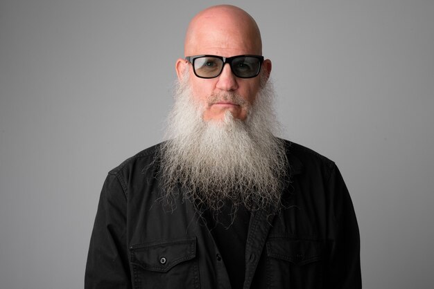 mature handsome bald man with long white beard against gray wall