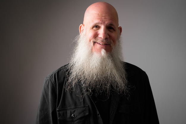 mature handsome bald man with long white beard against gray wall