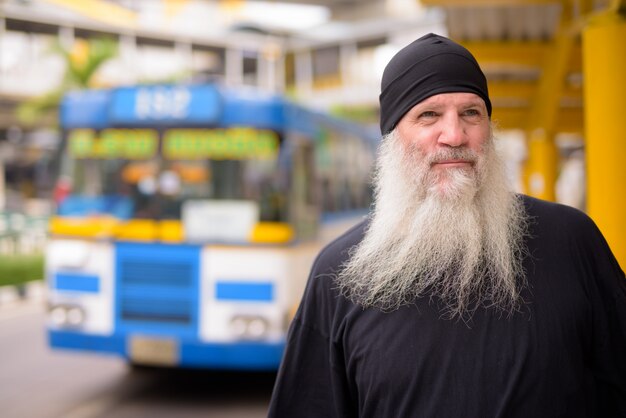 Mature handsome bearded hipster man thinking at the bus stop