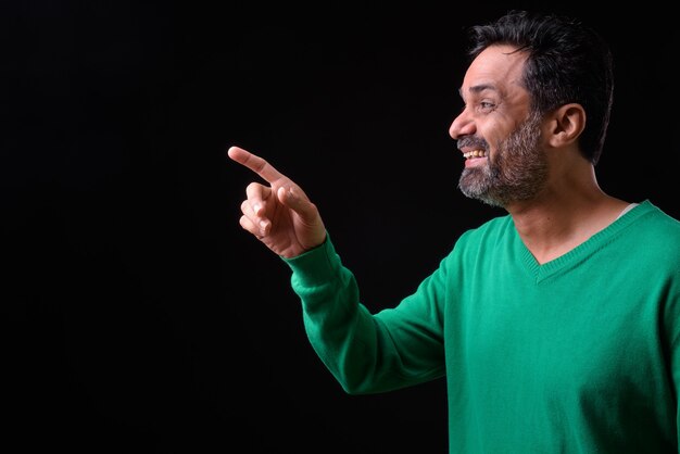  mature handsome bearded Indian man with curly hair against black wall