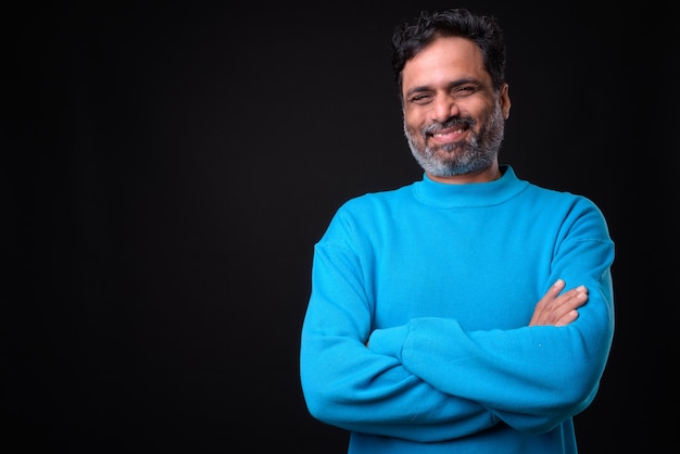  mature handsome bearded Indian man with curly hair against black wall