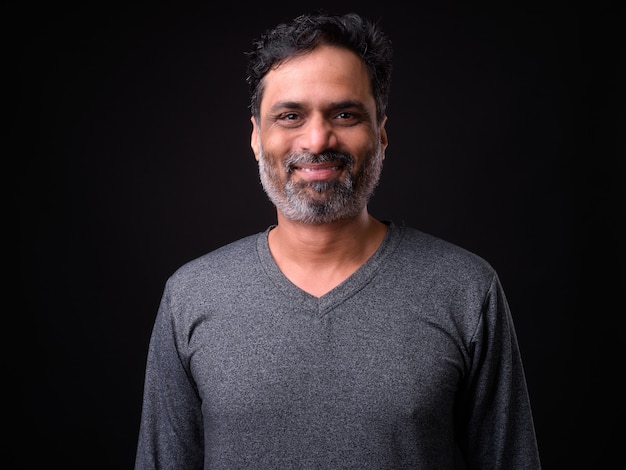  mature handsome bearded Indian man with curly hair against black wall