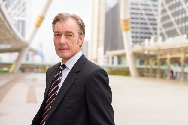 Mature handsome businessman in suit at skywalk bridge in the city