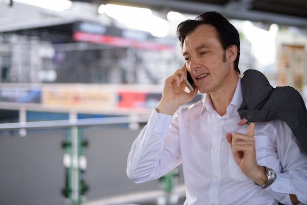 Зрелый красивый бизнесмен разговаривает по телефону на открытом воздухе
