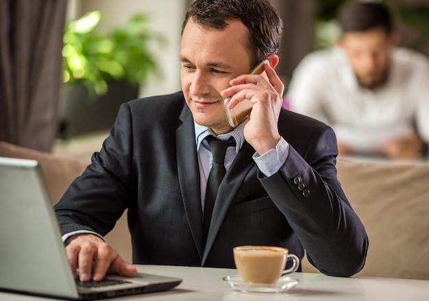 Mature handsome businessman using laptop and talking on the phone in cafe