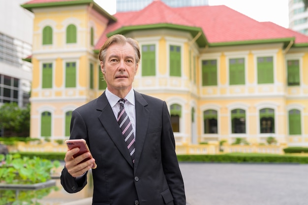 Foto uomo d'affari bello maturo utilizzando il telefono in città all'aperto