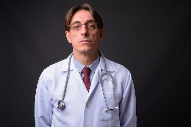 mature handsome Italian man doctor against gray wall