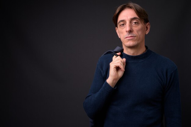 mature handsome Italian man wearing blue sweater against gray wall