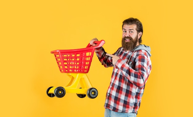 L'uomo bello maturo in camicia a scacchi porta il carrello della spesa compra