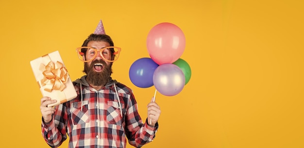 Mature handsome man in checkered shirt with party balloons and present box holiday