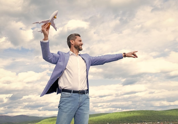 Mature happy man entrepreneur in jacket hold toy plane on sky background freedom