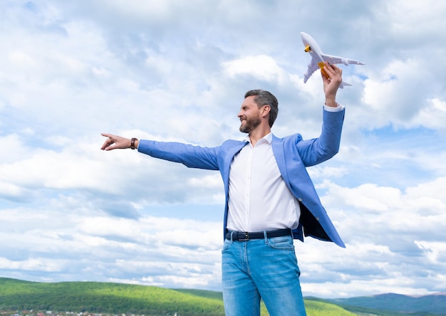 Mature happy man entrepreneur in jacket hold toy plane on sky background, freedom