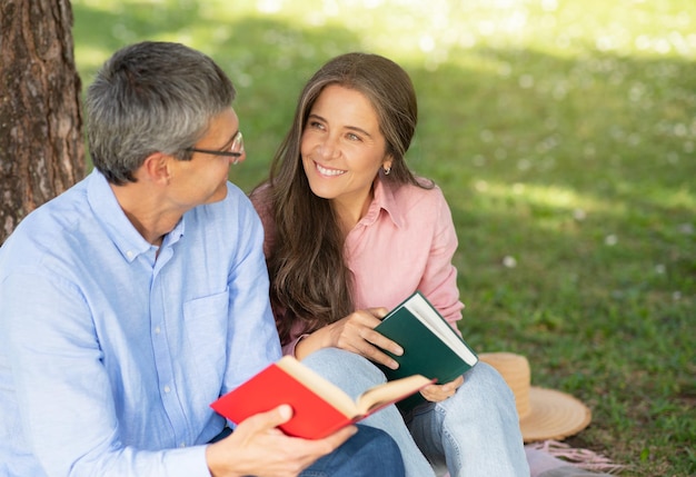 Foto marito e moglie maturi leggono un libro mentre si rilassano insieme nel parco