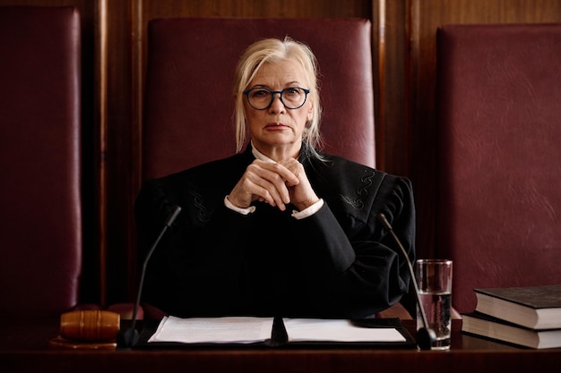 mature impartial female judge in eyeglasses and black mantle looking at camera