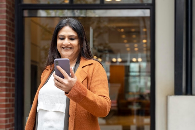 Mature Indian woman holding mobile phone reading text message standing on urban street