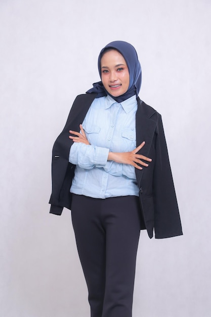 ヒジャブの青いシャツを着た成熟したインドネシアのオフィス女性が陽気な笑顔で腕を折りたたんで立っています