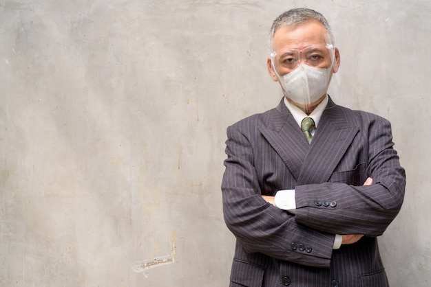 Mature Japanese businessman with mask and face shield crossing arms