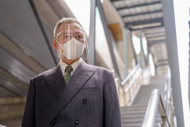 Mature Japanese businessman with mask and face shield going down the staircase