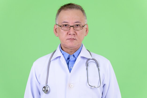  mature Japanese man doctor with eyeglasses against chroma key with green wall