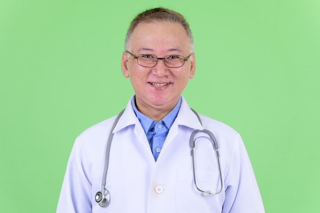 Photo mature japanese man doctor with eyeglasses against chroma key with green wall