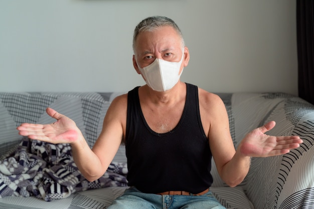 検疫下で自宅で肩をすくめマスクを持つ成熟した日本人男性