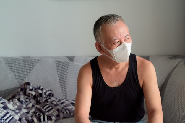 Mature Japanese man with mask sitting on the sofa at home under quarantine