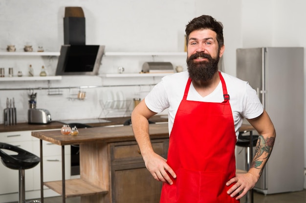 Mature male Bearded man cook Bearded man in red apron Restaurant or cafe cook Man chef cooking Hipster in kitchen satisfied chef in uniform apron Householding brings pleasure This is my place