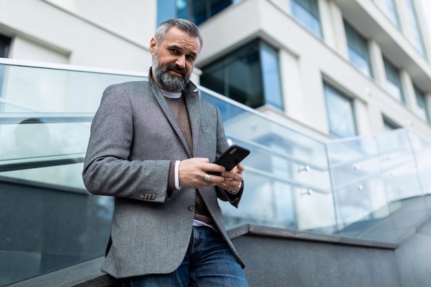 Mature male businessman in a classic gray jacket looks at the phone on the background of the