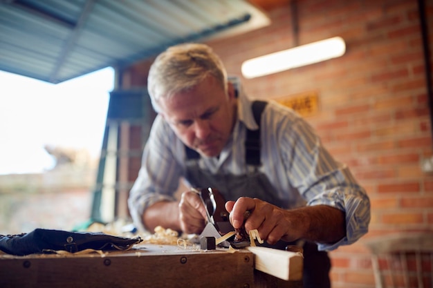 Carpentiere maschio maturo nel pezzo di legno di piallatura dell'officina del garage