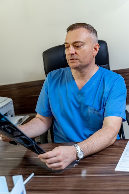 Mature male doctor looking at x-ray isolated on modern office backgound. Healthcare, roentgen, people and medicine concept.