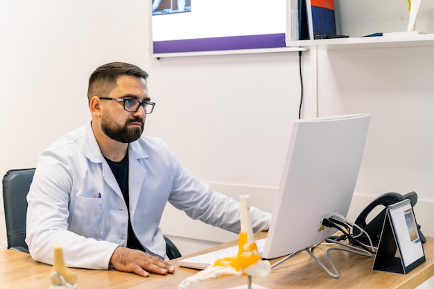 Mature male doctor working on laptop computer sitting in medical office