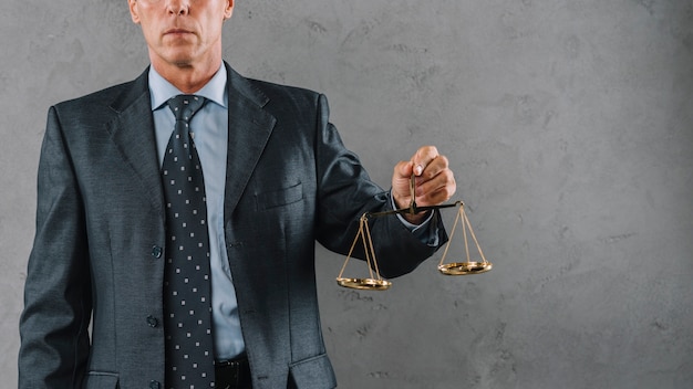 Mature male lawyer holding justice scale against gray textured background