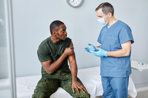 Mature male nurse giving recommendations to young black soldier after giving him vaccine injection a