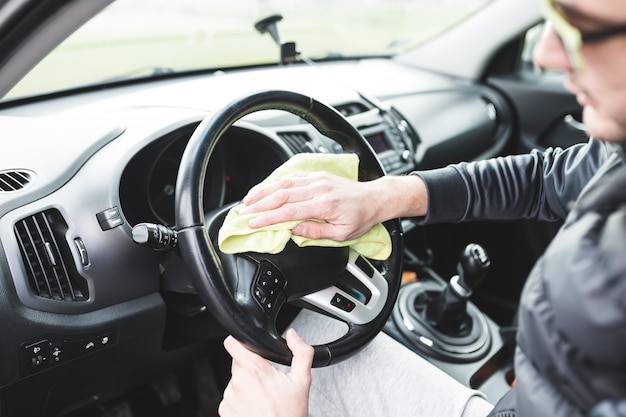 Maschio maturo con gli occhiali che puliscono il cruscotto dell'auto con un panno giallo