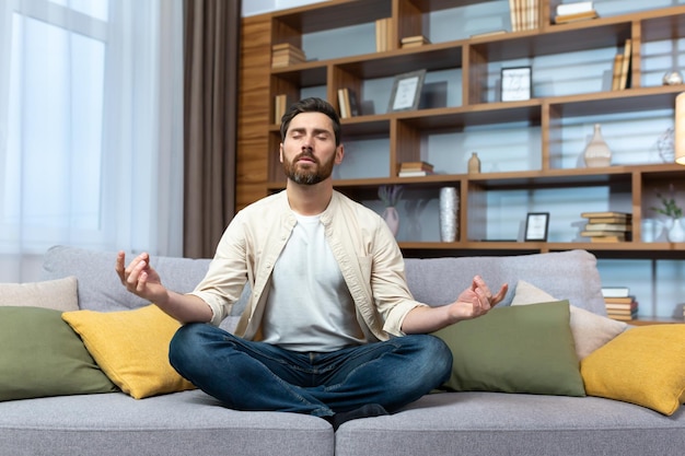 Mature man alone at home resting after work sitting in lotus position on sofa in living room